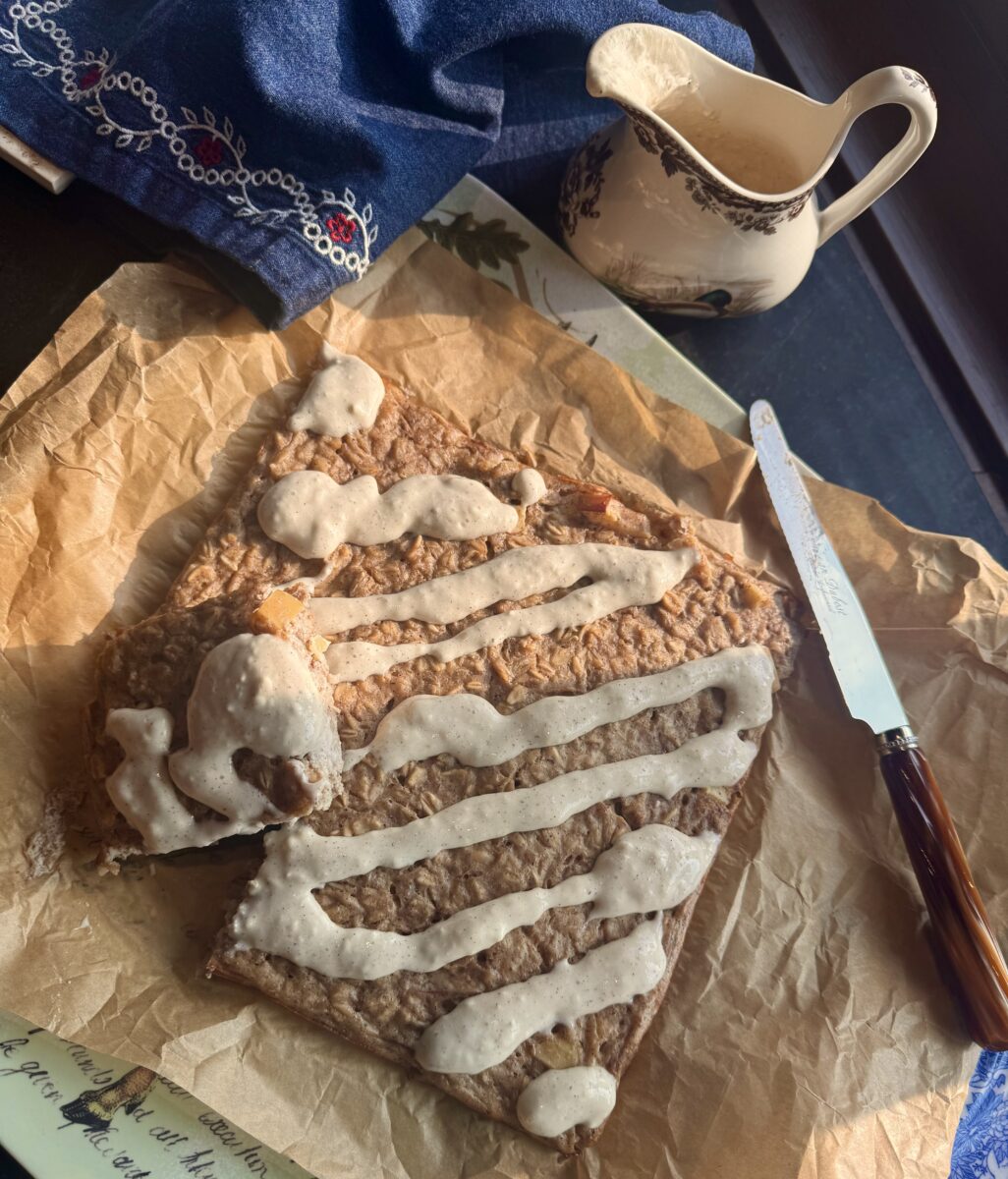 a square of high protein overnight oats drizzled with icing on a tray lined with parchment paper next to a denim blue napkin and a French knife with a brown resin handle 
